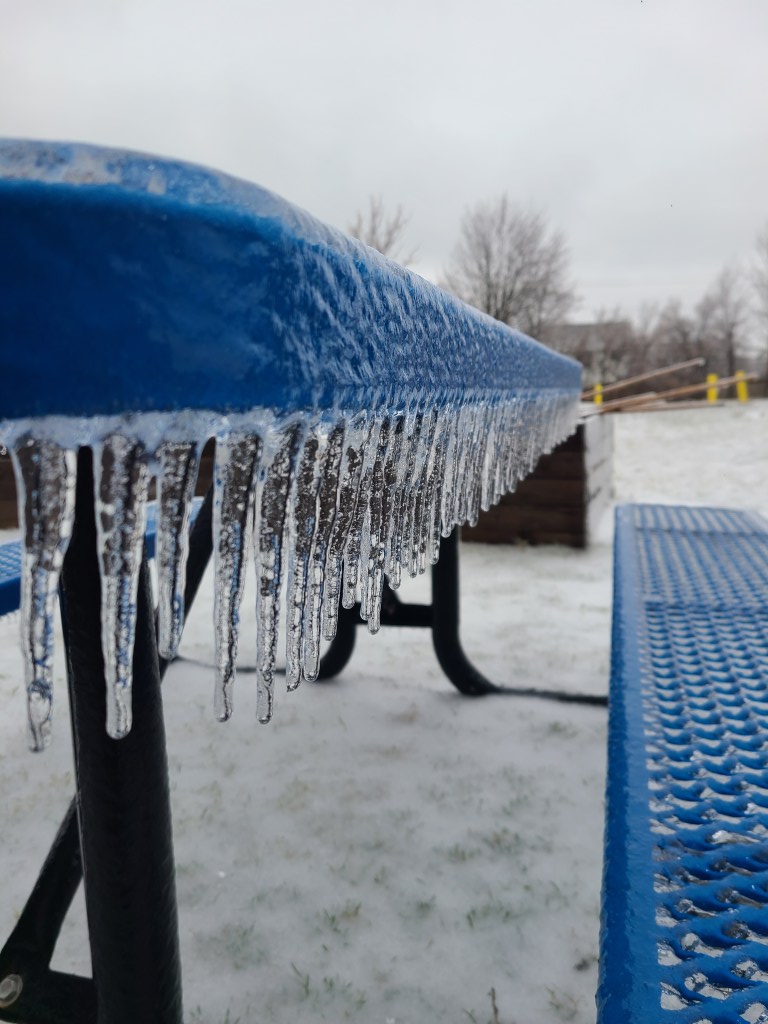 Photograph of icicles hanging from a picnic table outside. 