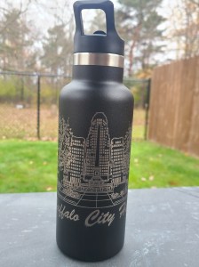 Photograph of engraved tumbler outside. Tumbler is engraved with a scene of Buffalo City Hall.