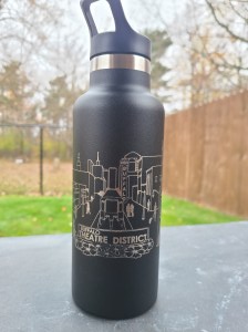 Photograph of engraved tumbler outside. Tumbler is engraved with a scene of the Theatre District in Buffalo, NY.