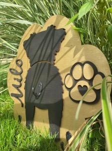 Photograph of multi-layered wooden sign that is in the shape of a paw print and has three hooks for holding leashes and other accessories.