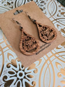 Photo of wooden teardrop shaped Buffalo Bills Earrings (Josh Allen) attached to a cardstock backer for hanging on display. This cardstock backer is stamped with the website and social media handle of the small business. Background is white with gold filigree design.
