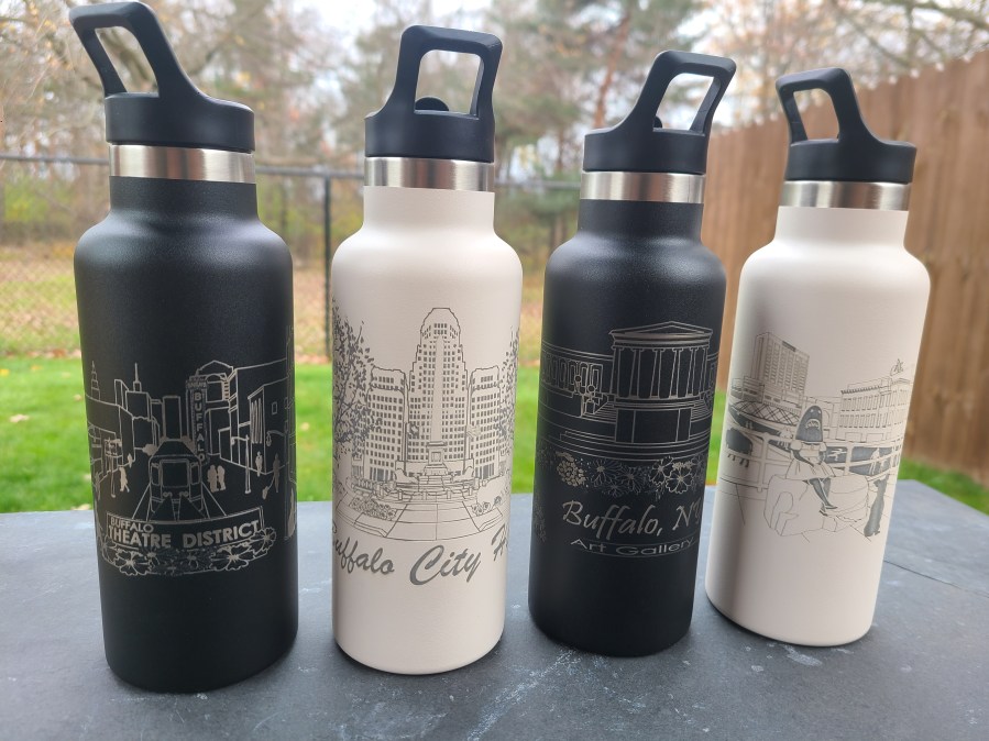 Photograph of four stainless steel tumblers in an outdoor setting. Photo features engraved tumblers with four different scenes from Buffalo, NY. Left to Right: Theatre District, Buffalo City Hall, Art Gallery, and Canalside.