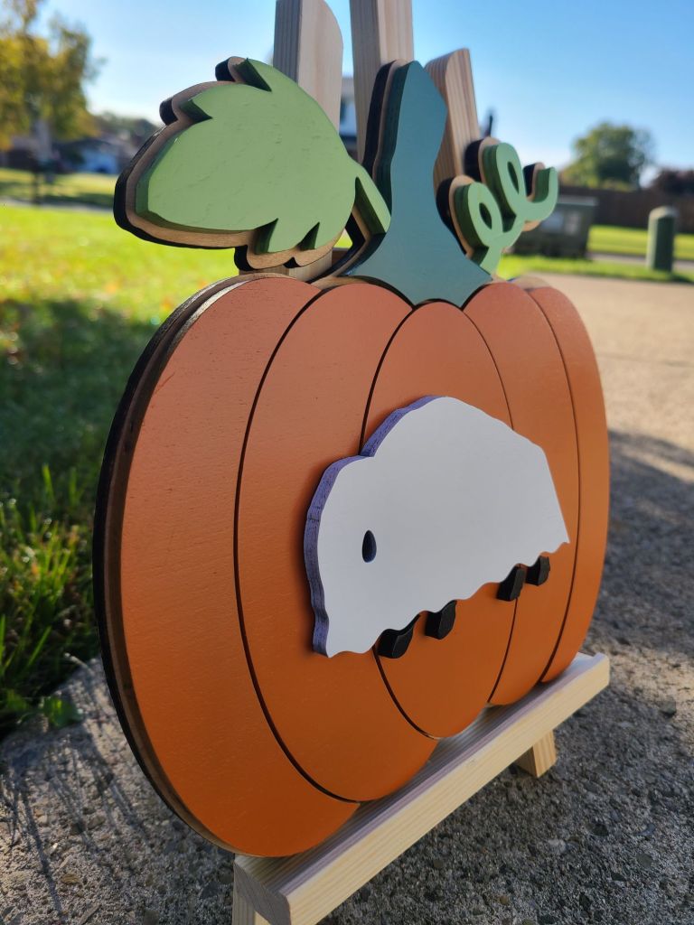 Photograph of layered wooden pumpkin sign with vibrant orange and greens. Buffalo dressed as a ghost is the top most layer.