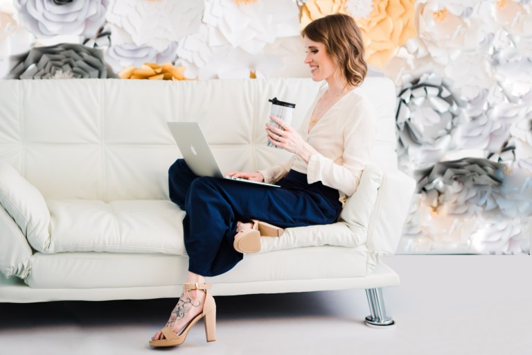 Photograph of business woman working on a couch with a laptop and a coffee.