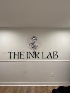 Photograph of Custom Acrylic signage - 1/4" with hidden standoffs for mounting. Reads "The Ink Lab" with their rose logo