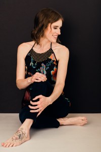 Professional Photograph of business owner sitting on ground, holding one knee and looking off to the side.