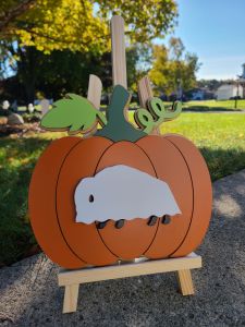 Photograph of layered wooden pumpkin sign with vibrant orange and greens. Buffalo dressed as a ghost is the top most layer.